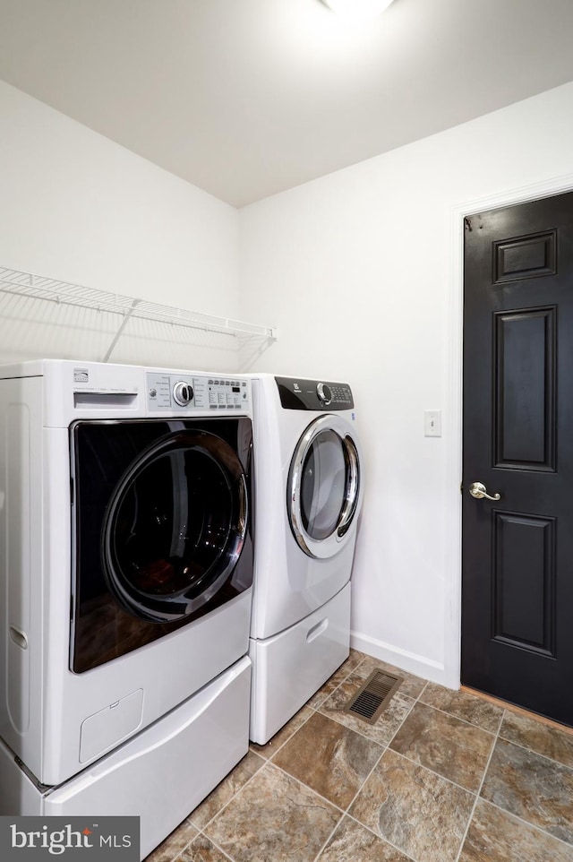 laundry area featuring baseboards, visible vents, washing machine and clothes dryer, laundry area, and stone finish floor