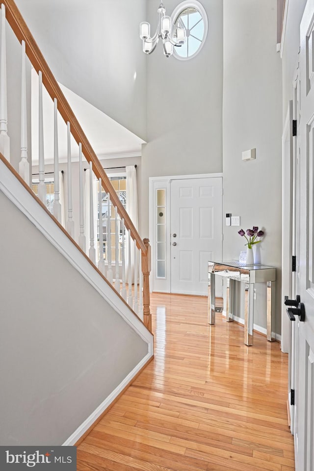 entryway featuring baseboards, wood finished floors, stairs, a towering ceiling, and an inviting chandelier