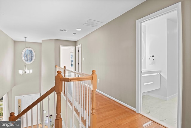 corridor featuring visible vents, baseboards, a chandelier, an upstairs landing, and light wood-style floors