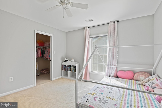 carpeted bedroom with a ceiling fan, visible vents, baseboards, a closet, and a walk in closet