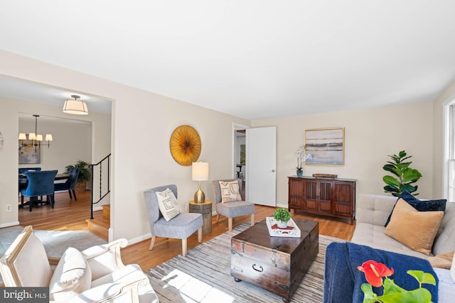 living area featuring stairway, baseboards, a notable chandelier, and light wood finished floors