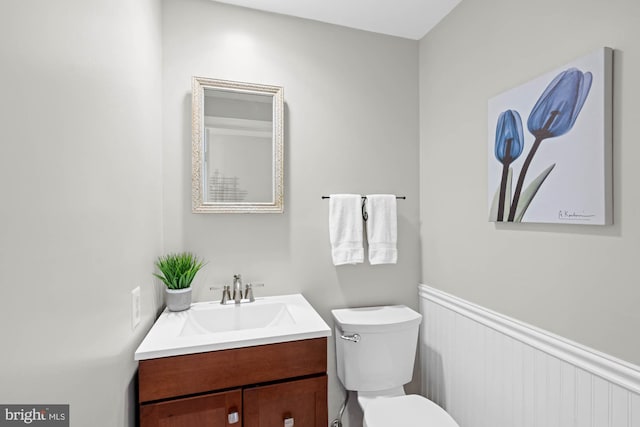 half bathroom with wainscoting, vanity, and toilet