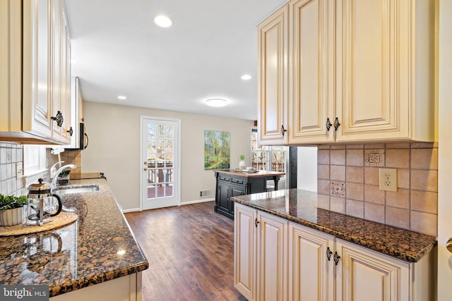 kitchen featuring dark stone countertops, baseboards, dark wood finished floors, a sink, and cream cabinets