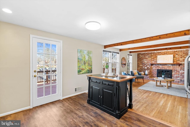 kitchen with visible vents, hardwood / wood-style flooring, beamed ceiling, dark cabinets, and a center island