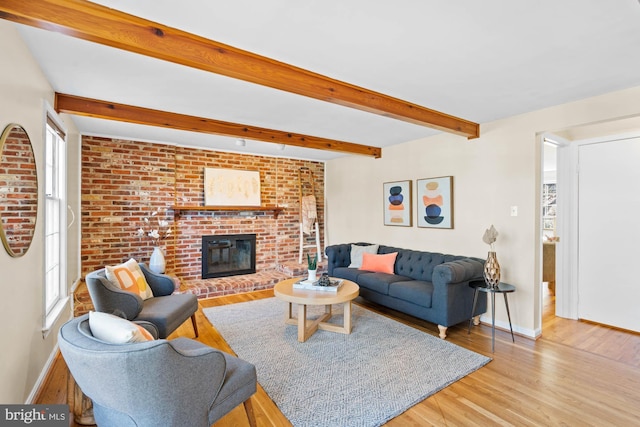 living area featuring beamed ceiling, wood finished floors, brick wall, baseboards, and a brick fireplace