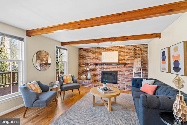 living room featuring beamed ceiling, a fireplace, baseboards, and wood finished floors