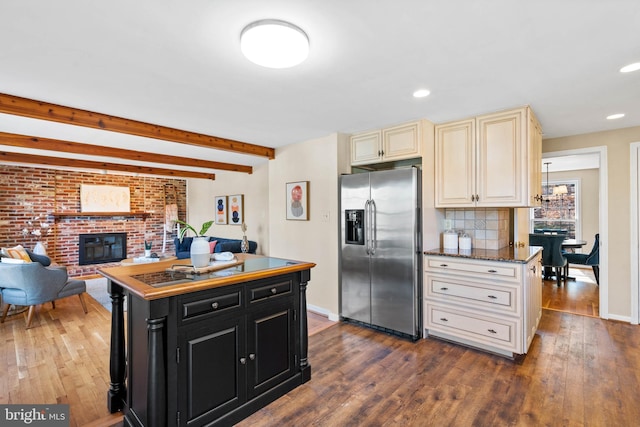 kitchen featuring cream cabinetry, stainless steel refrigerator with ice dispenser, dark wood finished floors, dark cabinetry, and a brick fireplace