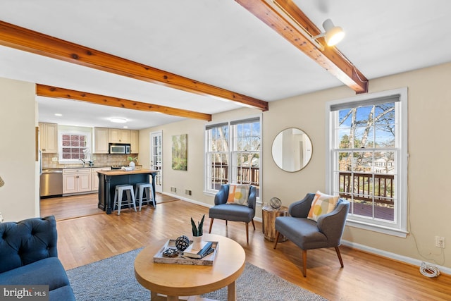 living area featuring beam ceiling, baseboards, light wood-type flooring, and a wealth of natural light