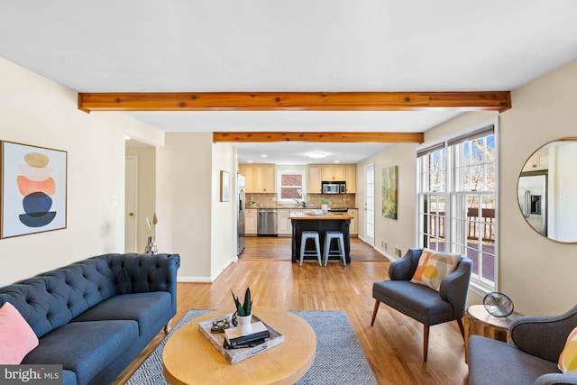 living area featuring beam ceiling, light wood finished floors, and baseboards