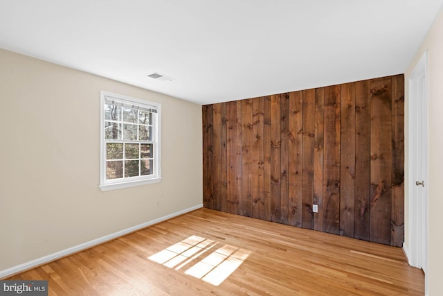 spare room with wooden walls, wood finished floors, visible vents, and baseboards