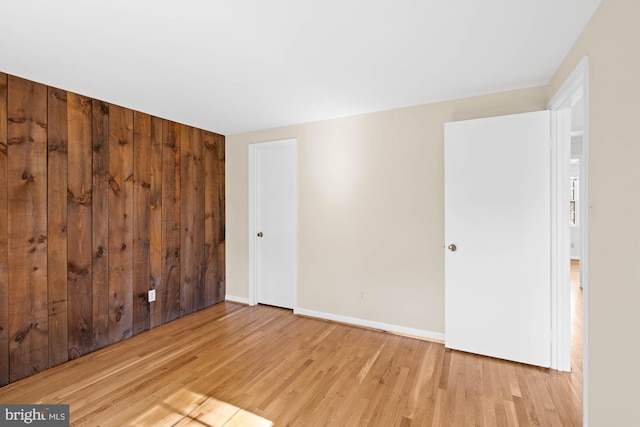 unfurnished room with baseboards, wood finished floors, and wood walls