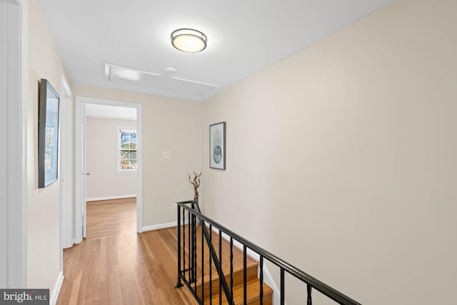 hall with baseboards, an upstairs landing, attic access, and light wood finished floors