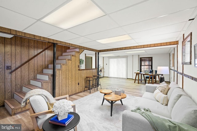 living room featuring stairway, a paneled ceiling, wood walls, and light wood-style flooring