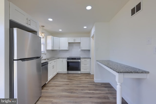 kitchen featuring visible vents, a sink, appliances with stainless steel finishes, white cabinets, and decorative backsplash