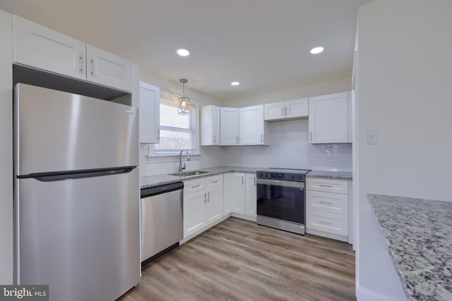 kitchen with light stone counters, a sink, stainless steel appliances, white cabinets, and light wood-type flooring