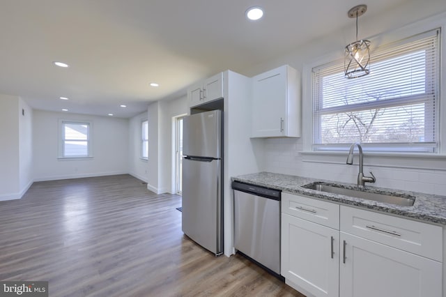 kitchen with a sink, white cabinets, light wood-style floors, appliances with stainless steel finishes, and tasteful backsplash