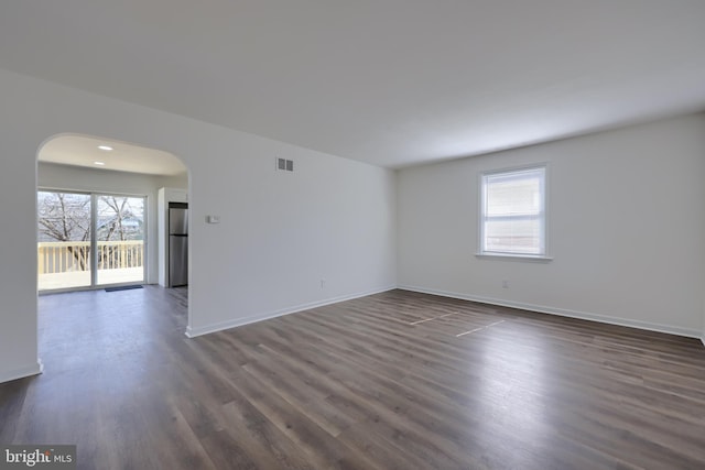 unfurnished room with arched walkways, visible vents, baseboards, and dark wood-style flooring