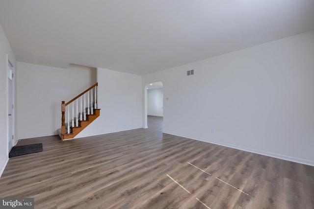 unfurnished living room with arched walkways, visible vents, stairs, and wood finished floors