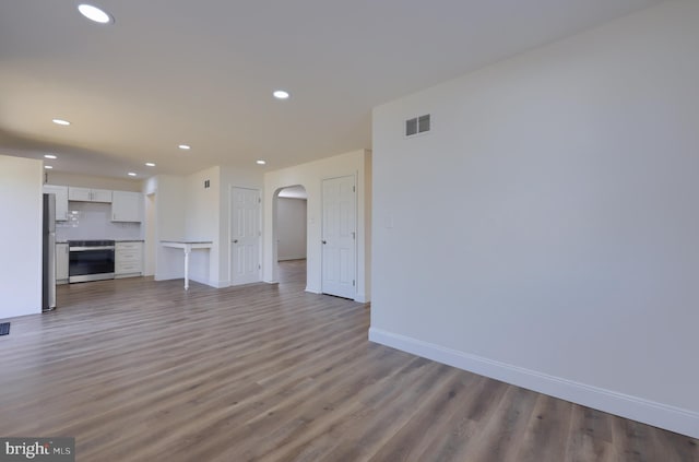 unfurnished living room featuring recessed lighting, visible vents, arched walkways, and wood finished floors