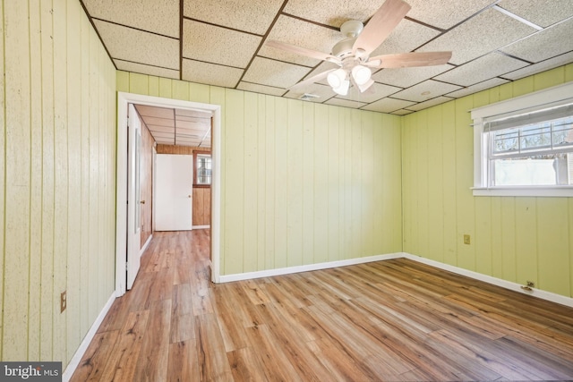 empty room with a ceiling fan, wood finished floors, baseboards, and a paneled ceiling