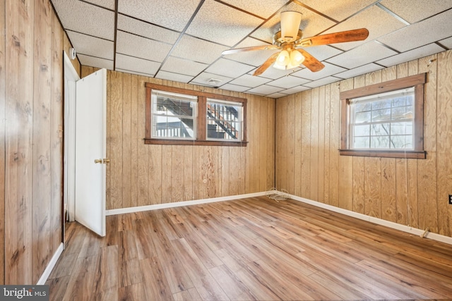 spare room featuring wooden walls, baseboards, a drop ceiling, wood finished floors, and a ceiling fan