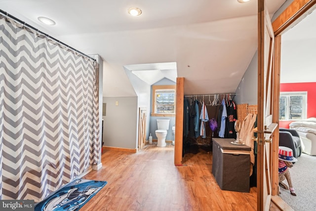 interior space featuring a closet, light wood-style floors, baseboards, an accent wall, and vaulted ceiling