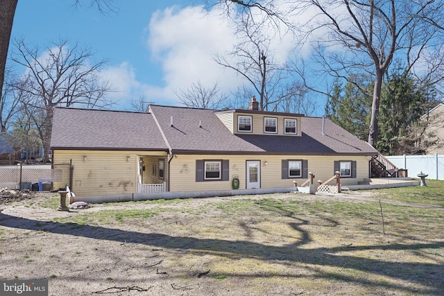 rear view of house featuring a yard, roof with shingles, a chimney, and fence