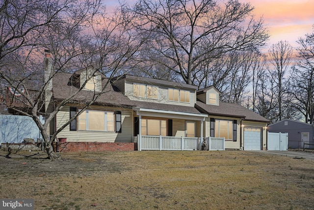 view of front of house with a lawn, fence, covered porch, a shingled roof, and a garage