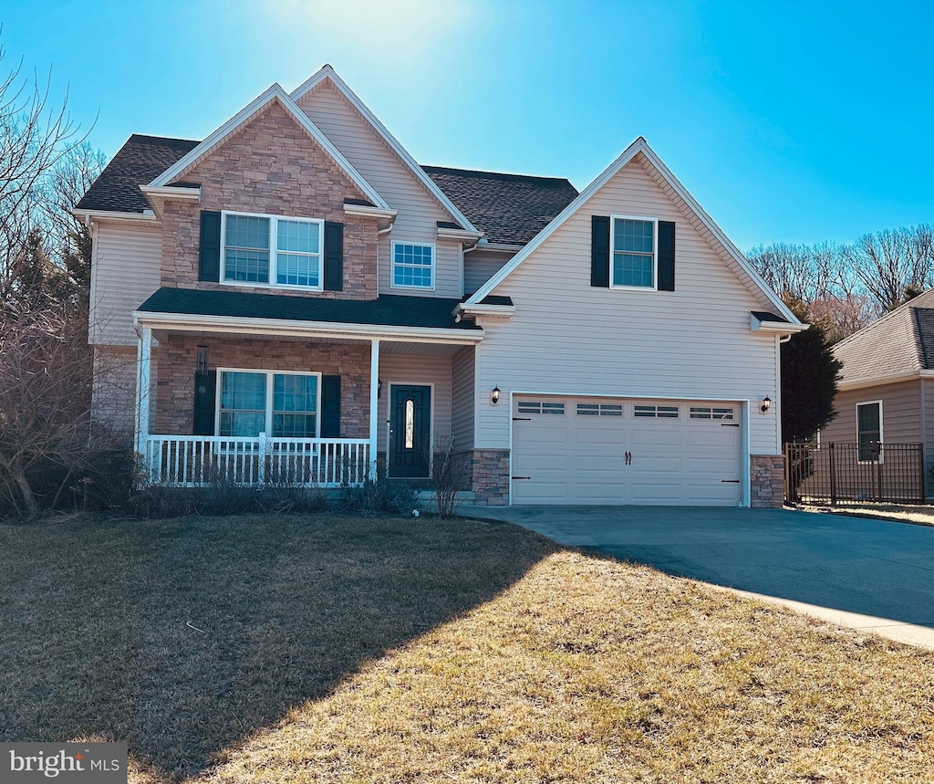 view of front facade with a front yard, an attached garage, covered porch, concrete driveway, and stone siding