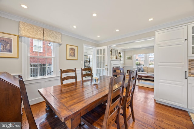 dining area featuring ornamental molding, wood finished floors, recessed lighting, wainscoting, and a fireplace