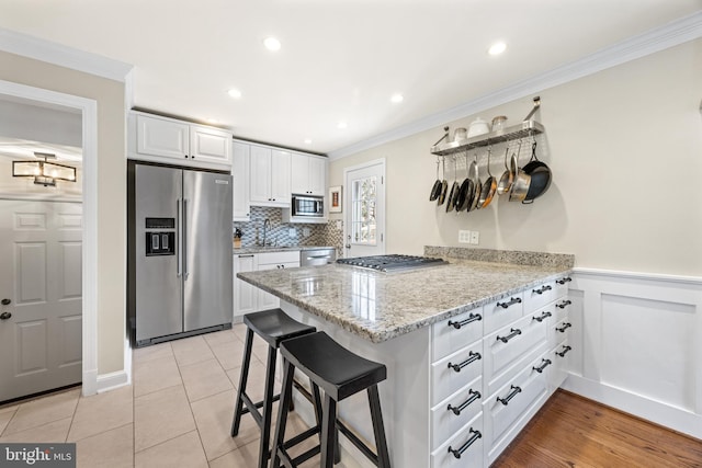 kitchen with ornamental molding, tasteful backsplash, appliances with stainless steel finishes, a peninsula, and white cabinets