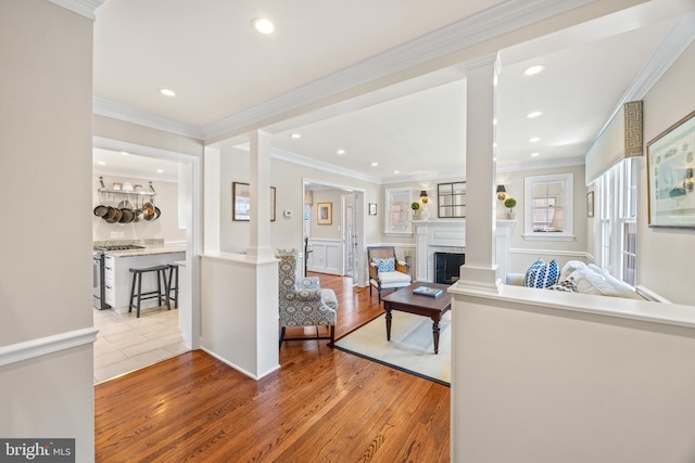 living room with decorative columns, light wood-style floors, a fireplace, and crown molding