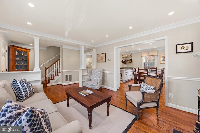 living room featuring visible vents, wood finished floors, crown molding, stairs, and ornate columns