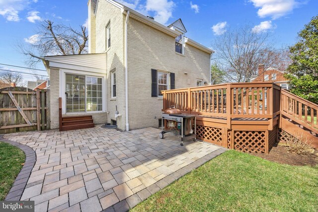 rear view of property featuring a gate, entry steps, a patio, a wooden deck, and brick siding