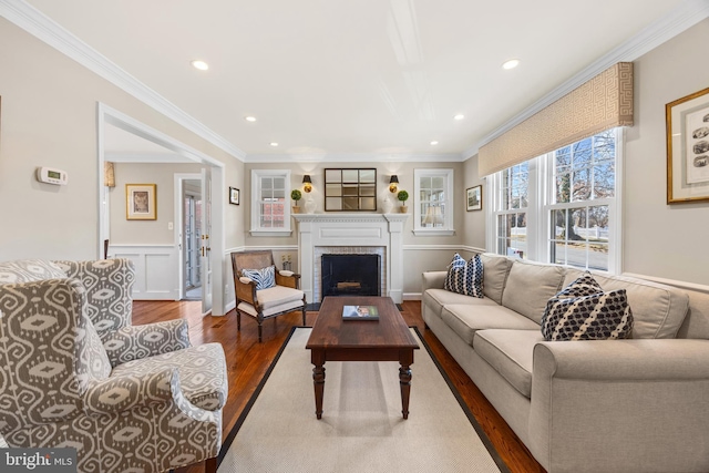 living area featuring wood finished floors, a fireplace, recessed lighting, wainscoting, and crown molding