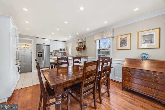 dining room with crown molding, recessed lighting, light wood-style floors, and a wainscoted wall