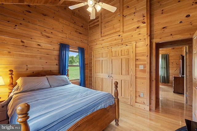 bedroom featuring high vaulted ceiling, wood walls, a ceiling fan, and light wood finished floors