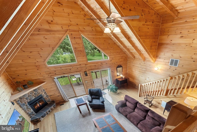 living room with wood ceiling, beamed ceiling, wooden walls, and a stone fireplace