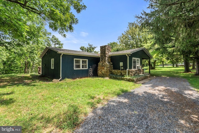 view of front of home featuring driveway, a chimney, and a front lawn