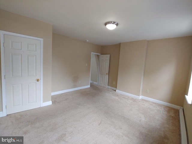 empty room with a baseboard heating unit, baseboards, and carpet floors