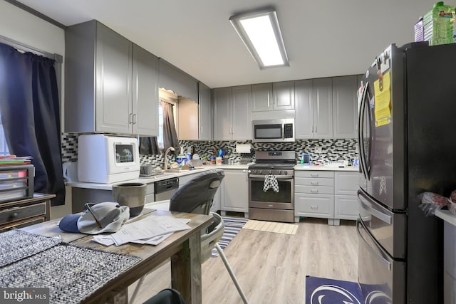 kitchen featuring light wood-type flooring, gray cabinetry, stainless steel appliances, light countertops, and decorative backsplash