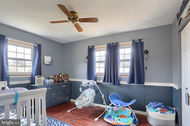 bedroom featuring a crib, a ceiling fan, baseboards, and wood finished floors