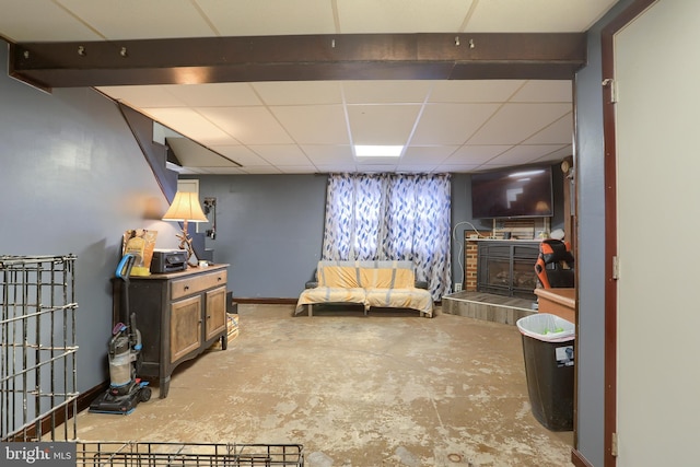 sitting room with a drop ceiling, unfinished concrete flooring, baseboards, and a tile fireplace