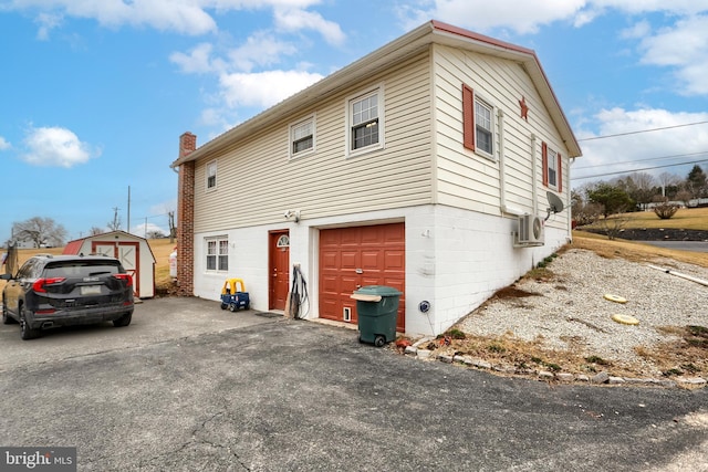 view of property exterior with ac unit, a chimney, driveway, an outbuilding, and an attached garage