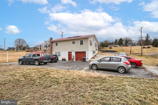 view of property exterior featuring driveway, a yard, a garage, solar panels, and a chimney