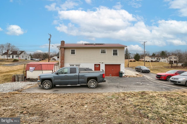 exterior space featuring aphalt driveway, an attached garage, roof mounted solar panels, and a chimney