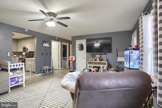 living room with baseboards, light wood-type flooring, and a ceiling fan