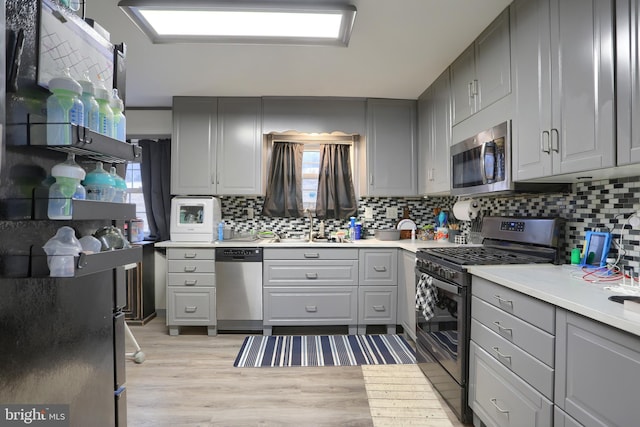 kitchen featuring backsplash, gray cabinetry, light countertops, appliances with stainless steel finishes, and a sink