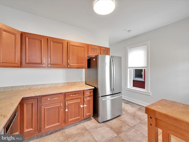 kitchen with light tile patterned floors, light stone countertops, brown cabinetry, and appliances with stainless steel finishes