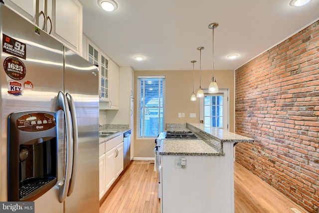 kitchen featuring white cabinetry, appliances with stainless steel finishes, brick wall, light wood finished floors, and glass insert cabinets